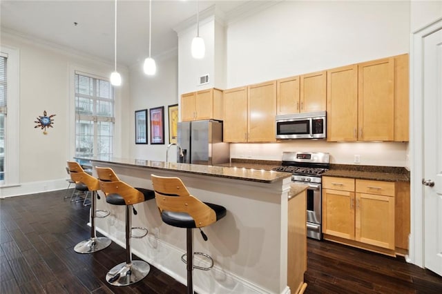 kitchen with stainless steel appliances, a breakfast bar, dark hardwood / wood-style flooring, hanging light fixtures, and a center island with sink