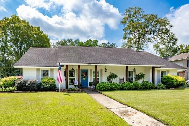 ranch-style house featuring covered porch, a shingled roof, and a front lawn