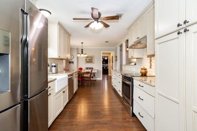 kitchen featuring pendant lighting, appliances with stainless steel finishes, white cabinetry, light stone countertops, and under cabinet range hood