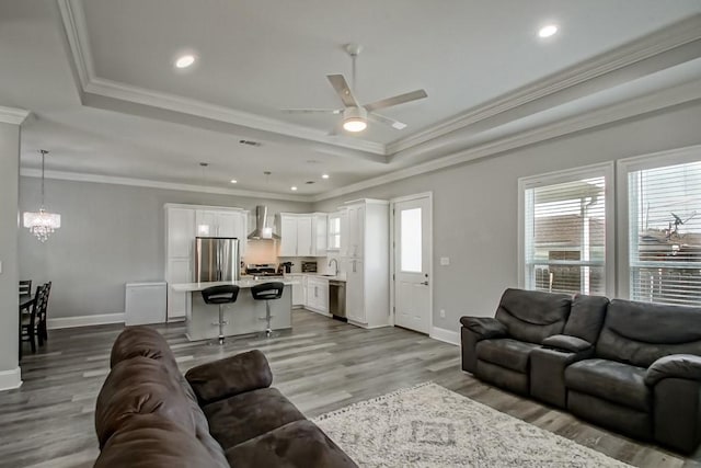 living room featuring ceiling fan with notable chandelier, light hardwood / wood-style flooring, a raised ceiling, and ornamental molding