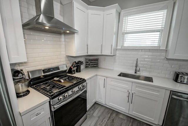 kitchen with sink, wall chimney range hood, white cabinetry, appliances with stainless steel finishes, and decorative backsplash