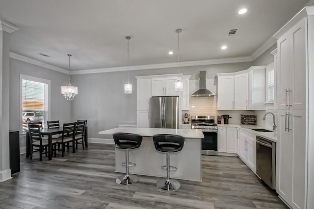 kitchen with wall chimney exhaust hood, appliances with stainless steel finishes, a center island, and white cabinetry