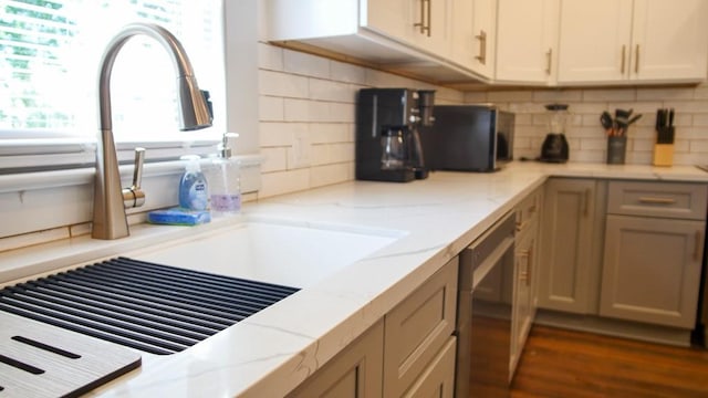 kitchen featuring light stone counters, tasteful backsplash, sink, dark hardwood / wood-style flooring, and dishwasher