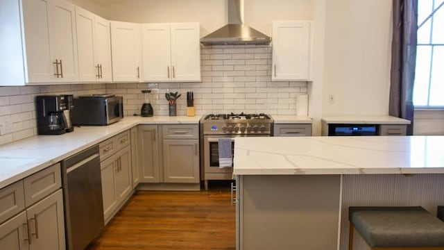 kitchen with wall chimney range hood, gray cabinetry, light stone countertops, dark hardwood / wood-style floors, and appliances with stainless steel finishes