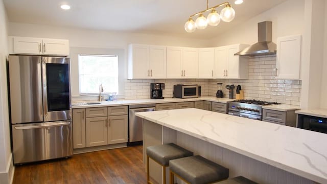 kitchen featuring wall chimney range hood, decorative light fixtures, light stone counters, stainless steel appliances, and white cabinets