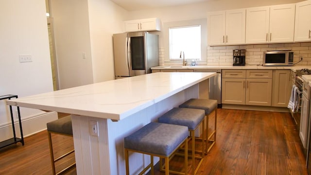 kitchen featuring a kitchen island, a kitchen breakfast bar, light stone counters, stainless steel appliances, and white cabinets