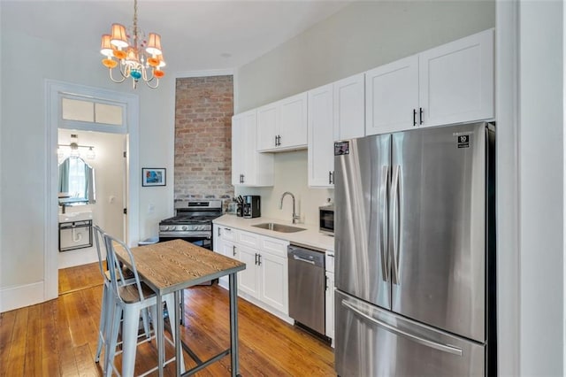 kitchen featuring white cabinets, sink, a chandelier, appliances with stainless steel finishes, and light hardwood / wood-style floors