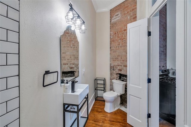 bathroom featuring toilet, brick wall, washer / dryer, crown molding, and hardwood / wood-style floors