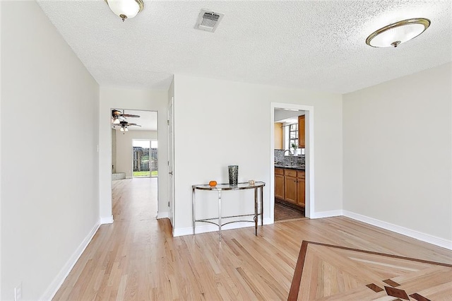 corridor with sink, a textured ceiling, and light hardwood / wood-style floors