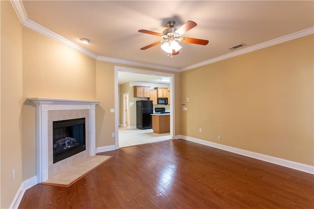 unfurnished living room featuring crown molding, ceiling fan, a tile fireplace, and wood-type flooring