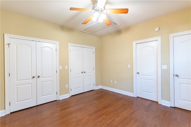 unfurnished bedroom with ceiling fan, multiple closets, and dark wood-type flooring