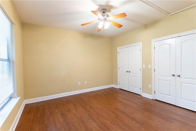 unfurnished bedroom with multiple closets, dark hardwood / wood-style flooring, and ceiling fan