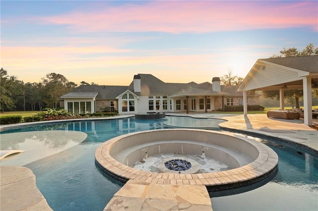 pool at dusk with an in ground hot tub and a patio