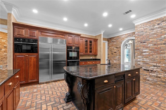 kitchen with built in fridge, an island with sink, brick wall, crown molding, and sink