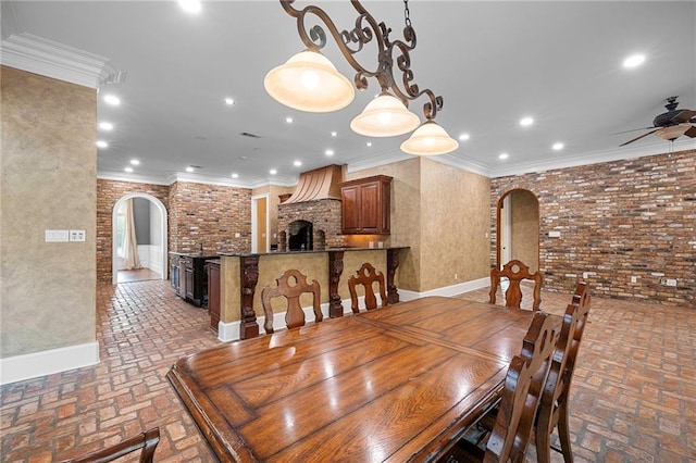 dining room with crown molding, brick wall, a fireplace, and ceiling fan