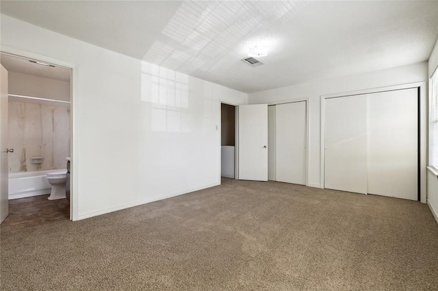 unfurnished bedroom featuring two closets, carpet floors, and ensuite bathroom