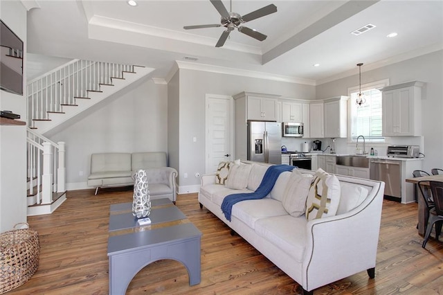 living room with dark hardwood / wood-style flooring, ceiling fan, crown molding, a tray ceiling, and sink