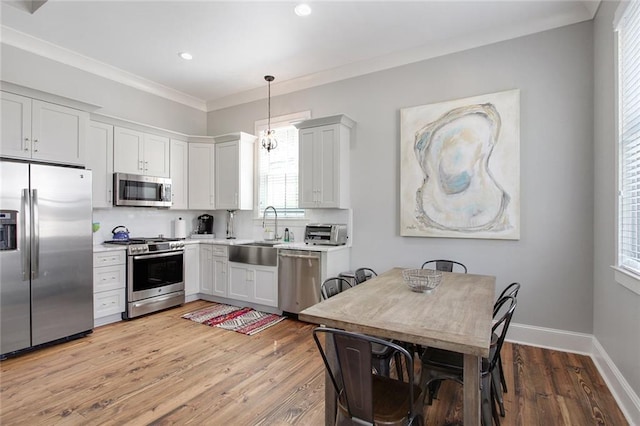 kitchen with light hardwood / wood-style flooring, stainless steel appliances, white cabinets, decorative light fixtures, and sink