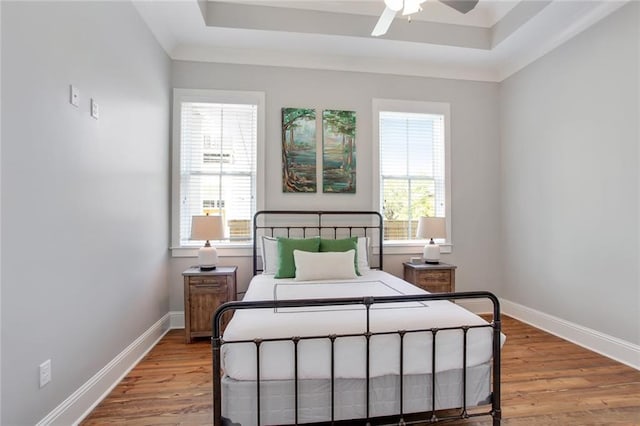 bedroom with light wood-type flooring and a tray ceiling