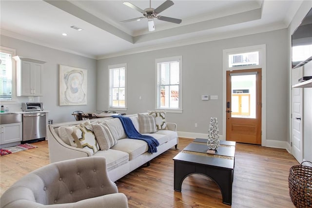 living room with a tray ceiling, ceiling fan, crown molding, and light hardwood / wood-style floors