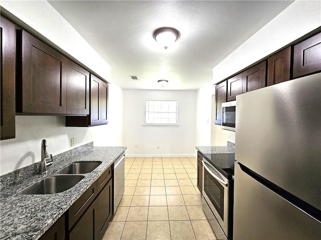 kitchen featuring dark stone countertops, dark brown cabinetry, stainless steel appliances, and sink