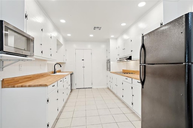 kitchen featuring white cabinets, light tile patterned floors, appliances with stainless steel finishes, sink, and butcher block countertops