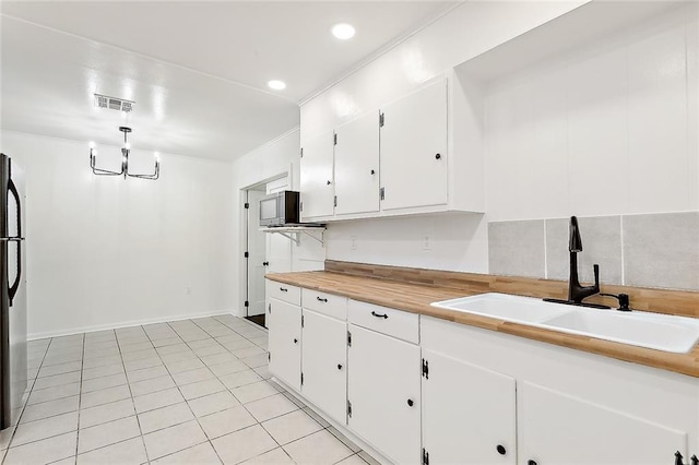 kitchen with white cabinets, light tile patterned flooring, stainless steel appliances, a notable chandelier, and sink