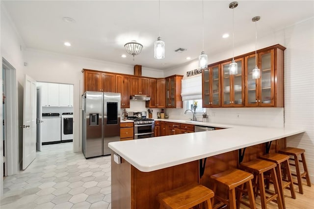 kitchen featuring a kitchen breakfast bar, kitchen peninsula, stainless steel appliances, pendant lighting, and washing machine and clothes dryer