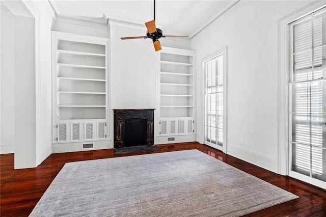 living room featuring a fireplace, dark wood-type flooring, crown molding, built in shelves, and ceiling fan