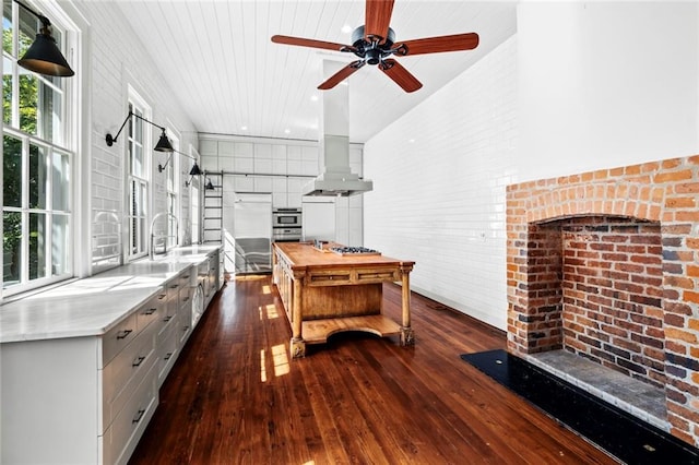 kitchen featuring wooden counters, wall chimney range hood, stainless steel appliances, sink, and dark hardwood / wood-style flooring