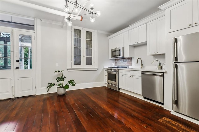 kitchen with appliances with stainless steel finishes, white cabinetry, decorative backsplash, a chandelier, and dark hardwood / wood-style floors