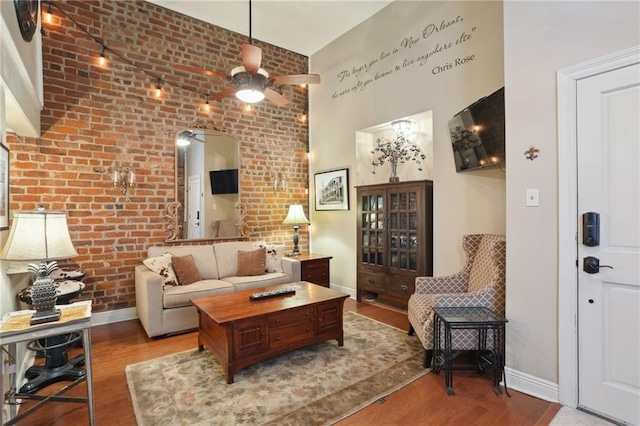 living room with ceiling fan, brick wall, a towering ceiling, and wood-type flooring