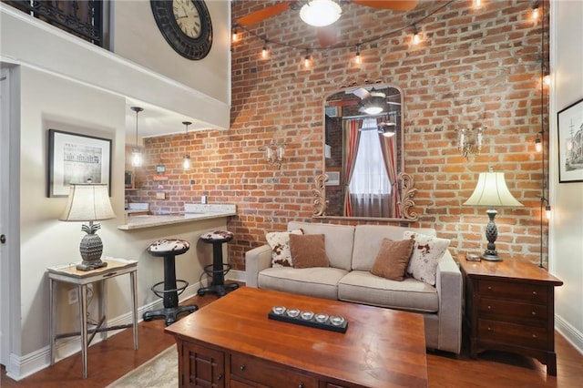living room featuring brick wall, ceiling fan, baseboards, and wood finished floors