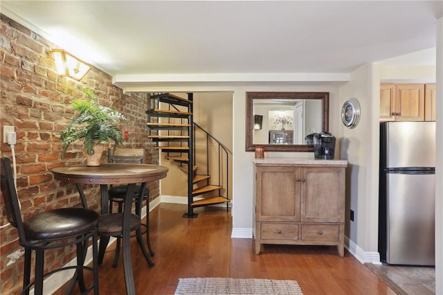 dining room featuring stairway, baseboards, dark wood-style flooring, and brick wall