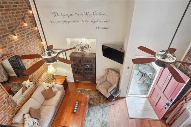 unfurnished room featuring ceiling fan, brick wall, light hardwood / wood-style flooring, and a high ceiling