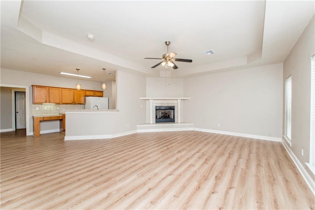 unfurnished living room featuring light hardwood / wood-style floors, a tray ceiling, a fireplace, and ceiling fan