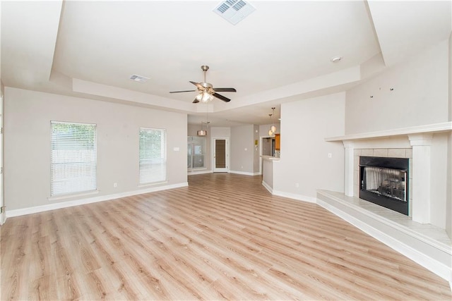 unfurnished living room featuring a tile fireplace, a tray ceiling, light hardwood / wood-style floors, and ceiling fan