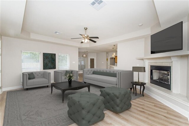 605 Florida St, Mandeville, LA 70448 - living room featuring a raised ceiling, light wood-style flooring, baseboards, ceiling fan, and a tiled fireplace