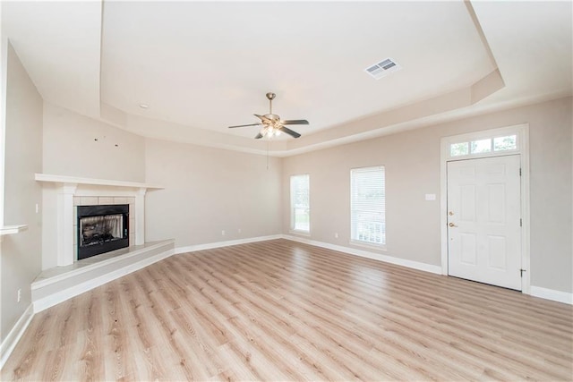 unfurnished living room with a tiled fireplace, a tray ceiling, a healthy amount of sunlight, and light hardwood / wood-style flooring