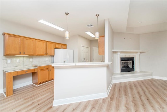 kitchen with decorative backsplash, kitchen peninsula, white refrigerator, a fireplace, and light hardwood / wood-style floors