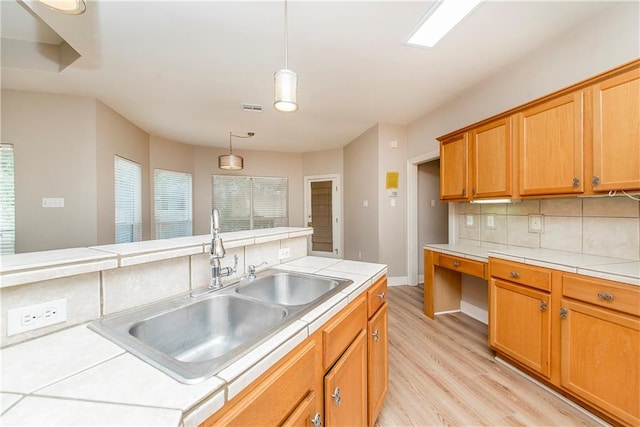 kitchen with tile countertops, sink, decorative light fixtures, and light hardwood / wood-style floors