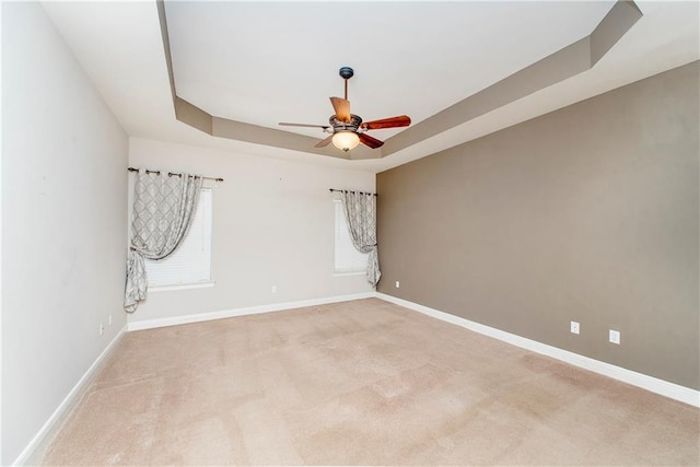 unfurnished room featuring light carpet, a tray ceiling, and ceiling fan