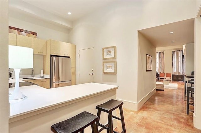 kitchen featuring sink, a kitchen breakfast bar, kitchen peninsula, stainless steel refrigerator, and cream cabinets