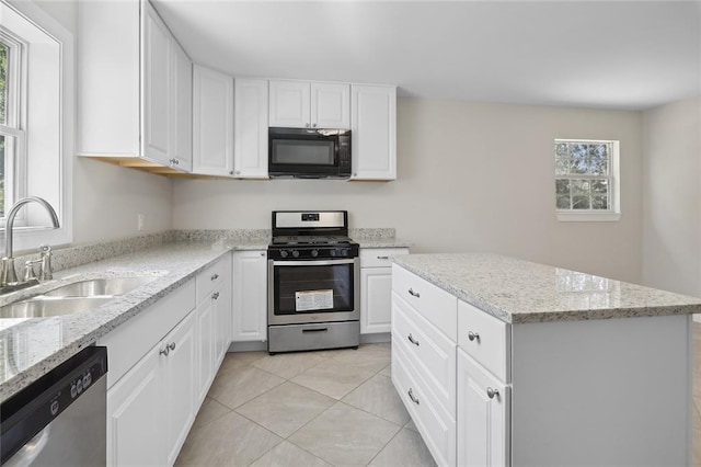 kitchen with stainless steel appliances, sink, a center island, white cabinetry, and light stone counters