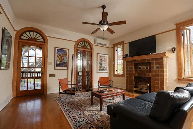 living room with ceiling fan, a wall mounted AC, dark hardwood / wood-style flooring, and a tile fireplace