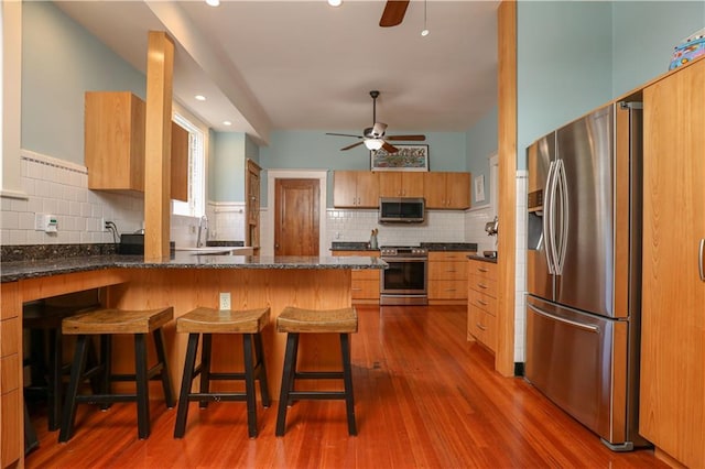 kitchen featuring wood-type flooring, appliances with stainless steel finishes, a breakfast bar, and kitchen peninsula