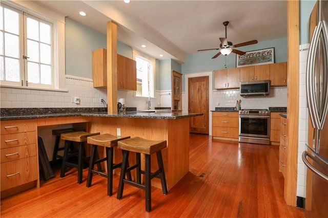 kitchen with wood-type flooring, kitchen peninsula, stainless steel appliances, decorative backsplash, and a breakfast bar