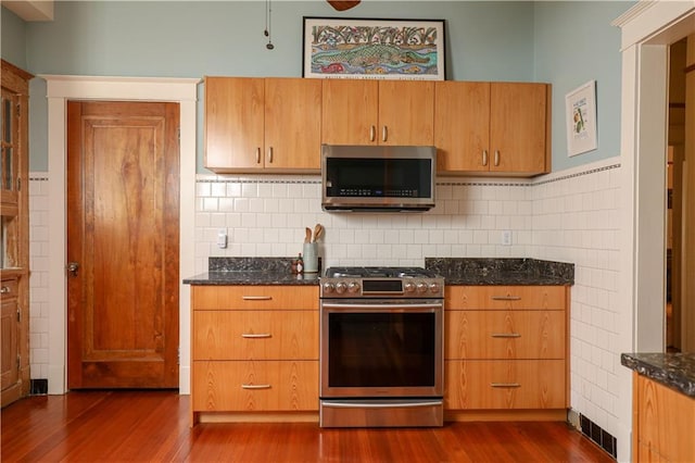 kitchen featuring tasteful backsplash, stainless steel appliances, dark wood-type flooring, and dark stone counters