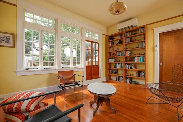 sitting room with an AC wall unit and wood-type flooring