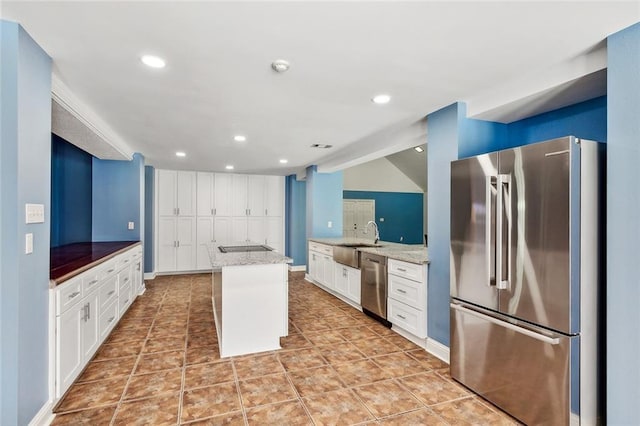 kitchen with a kitchen island, appliances with stainless steel finishes, a breakfast bar, white cabinetry, and light stone counters